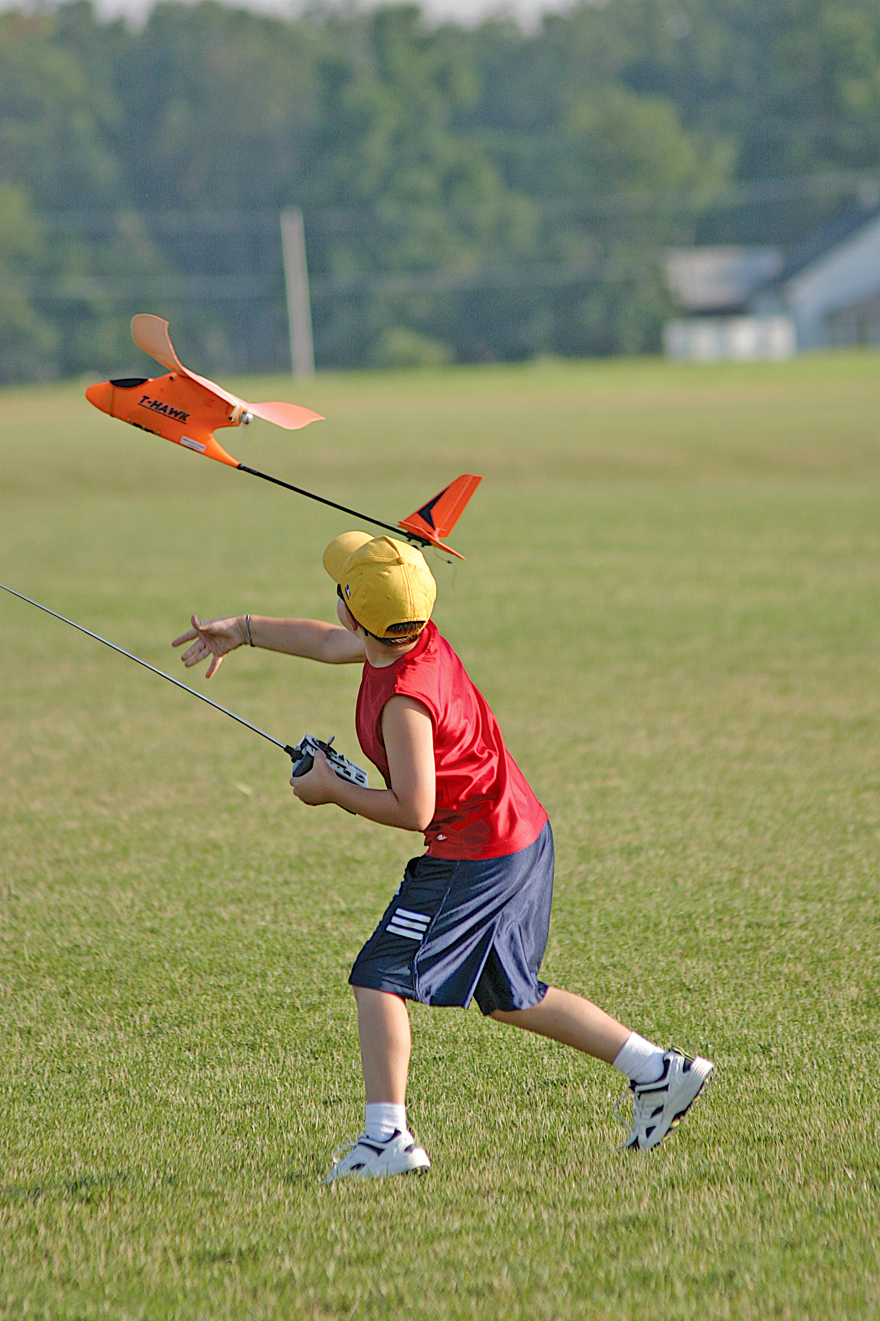 Boy flying an orange remote-controlled plane in a grassy field.